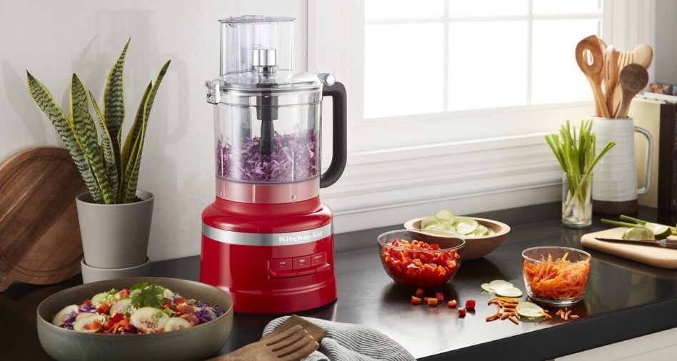 A red KitchenAid® food processor work bowl filled with shredded cabbage.